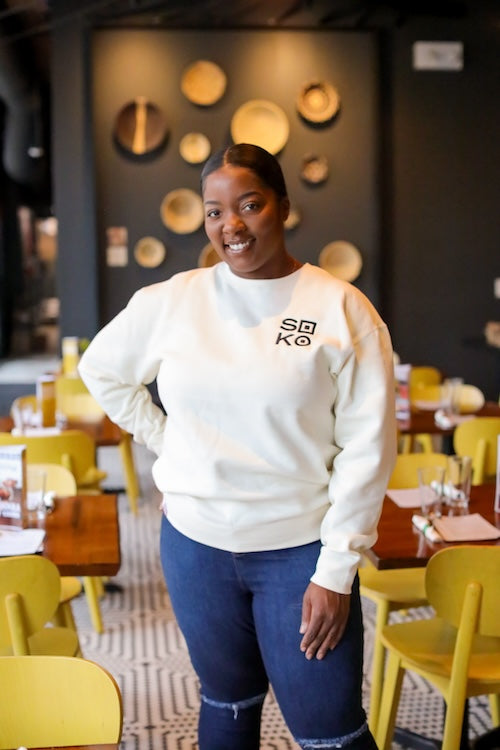 Woman wearing white sweatshirt with black embroidered Soko logo